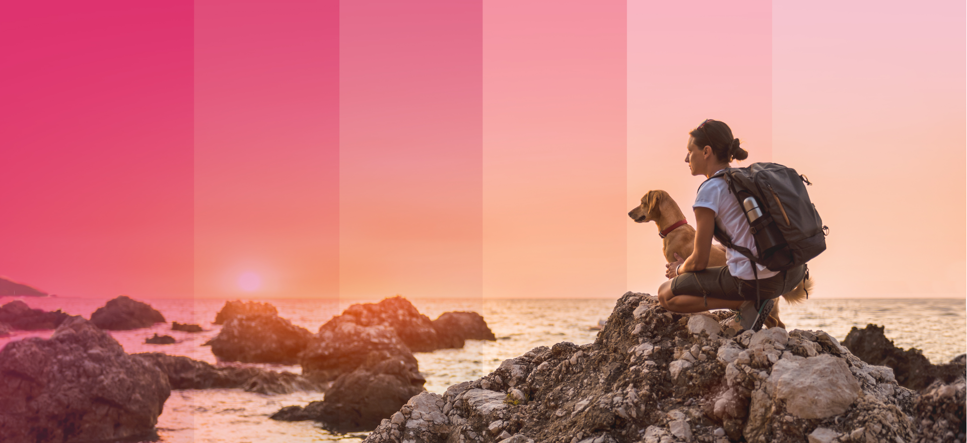 Woman and dog crouched on rocks looking at sunset